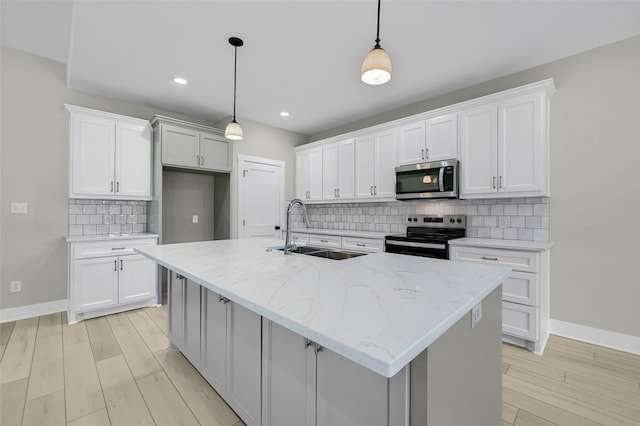 kitchen with hanging light fixtures, sink, an island with sink, appliances with stainless steel finishes, and white cabinetry