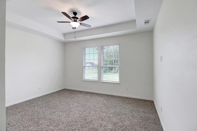 carpeted empty room featuring ceiling fan and a raised ceiling