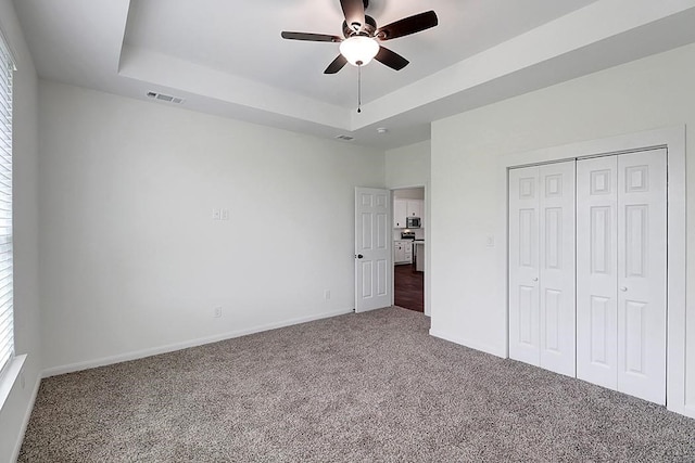 unfurnished bedroom with a closet, carpet floors, a tray ceiling, and ceiling fan