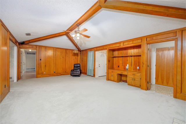 interior space featuring light carpet, lofted ceiling with beams, ceiling fan, a textured ceiling, and wood walls