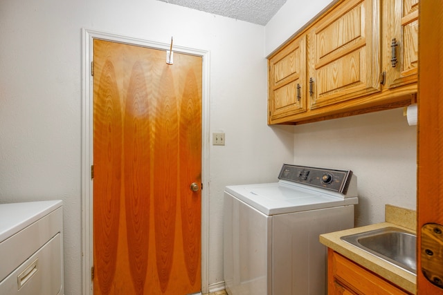 clothes washing area featuring sink, washing machine and clothes dryer, a textured ceiling, and cabinets