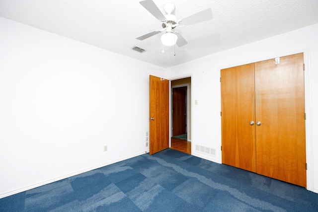 unfurnished bedroom featuring a closet, a textured ceiling, dark carpet, and ceiling fan