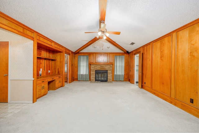 unfurnished living room with lofted ceiling with beams, ceiling fan, light colored carpet, a textured ceiling, and wood walls