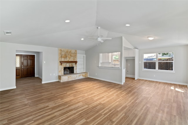 unfurnished living room featuring light hardwood / wood-style floors, lofted ceiling, a stone fireplace, and ceiling fan