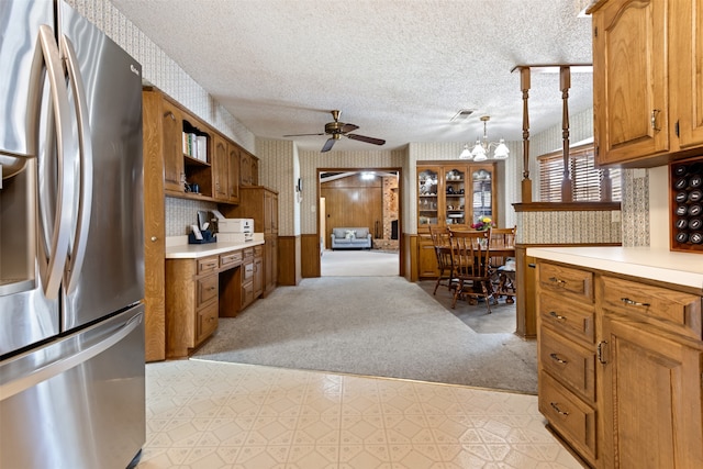 kitchen with light carpet, a textured ceiling, stainless steel refrigerator, ceiling fan with notable chandelier, and pendant lighting