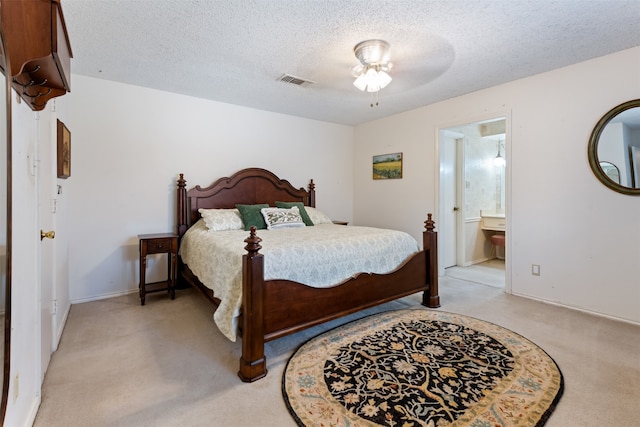 carpeted bedroom with a textured ceiling, ensuite bathroom, and ceiling fan