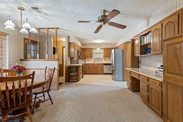 kitchen with built in desk, light carpet, decorative light fixtures, appliances with stainless steel finishes, and a textured ceiling