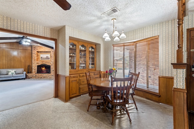 carpeted dining area with wood walls, a textured ceiling, ceiling fan with notable chandelier, and vaulted ceiling