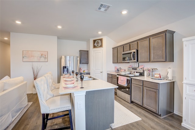 kitchen with an island with sink, sink, hardwood / wood-style floors, a kitchen bar, and appliances with stainless steel finishes