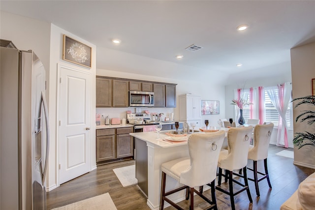 kitchen with a kitchen breakfast bar, an island with sink, stainless steel appliances, and dark hardwood / wood-style flooring