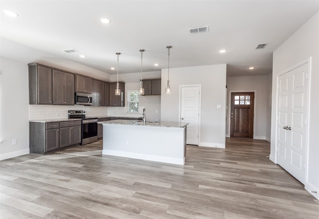 kitchen featuring an island with sink, light stone counters, stainless steel appliances, and light wood-type flooring