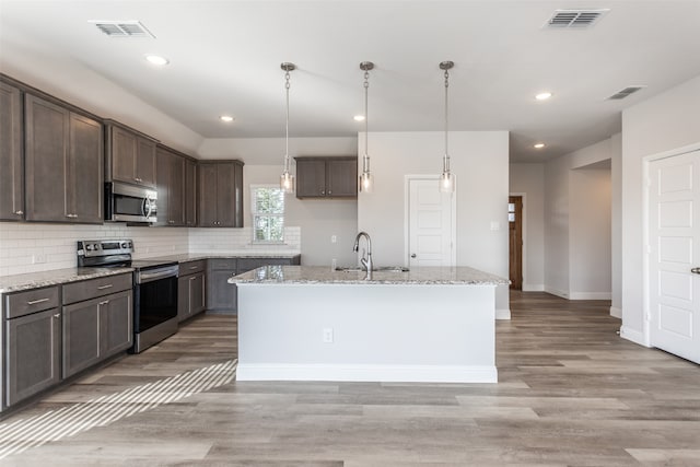 kitchen featuring light stone countertops, appliances with stainless steel finishes, light wood-type flooring, pendant lighting, and a center island with sink