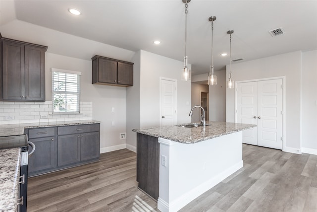 kitchen with hanging light fixtures, light stone counters, a kitchen island with sink, light hardwood / wood-style floors, and sink