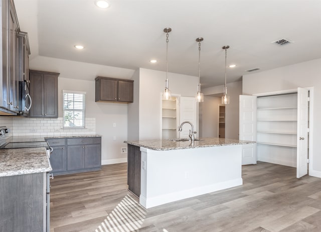 kitchen featuring light stone countertops, hanging light fixtures, a center island with sink, and light wood-type flooring