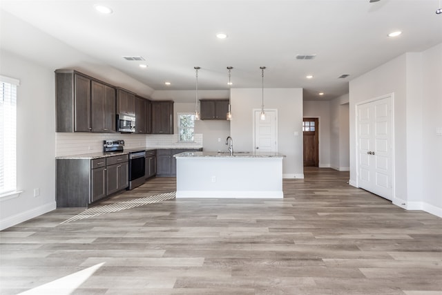 kitchen with a wealth of natural light, a kitchen island with sink, light stone countertops, and stainless steel appliances