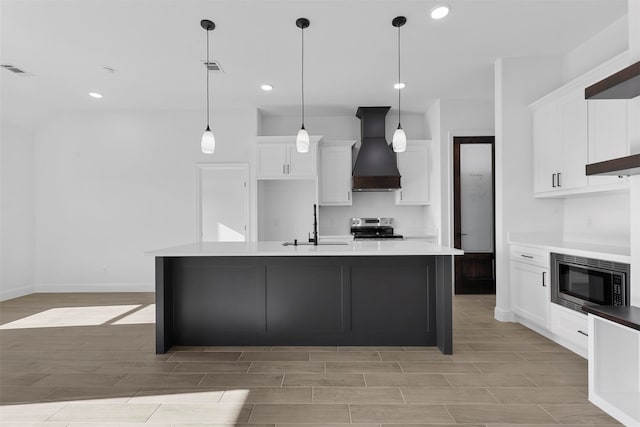 kitchen featuring an island with sink, pendant lighting, white cabinetry, custom exhaust hood, and appliances with stainless steel finishes