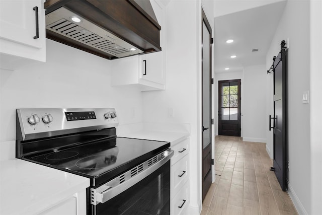 kitchen with a barn door, electric stove, white cabinetry, light hardwood / wood-style floors, and custom range hood