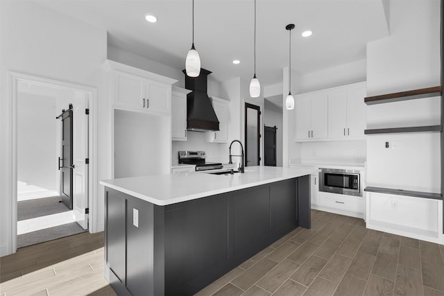 kitchen featuring hardwood / wood-style floors, appliances with stainless steel finishes, white cabinetry, a kitchen island with sink, and custom range hood