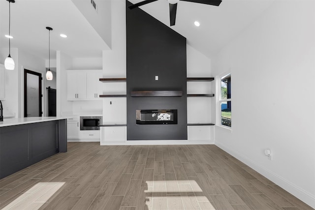 unfurnished living room featuring light hardwood / wood-style floors, high vaulted ceiling, and ceiling fan