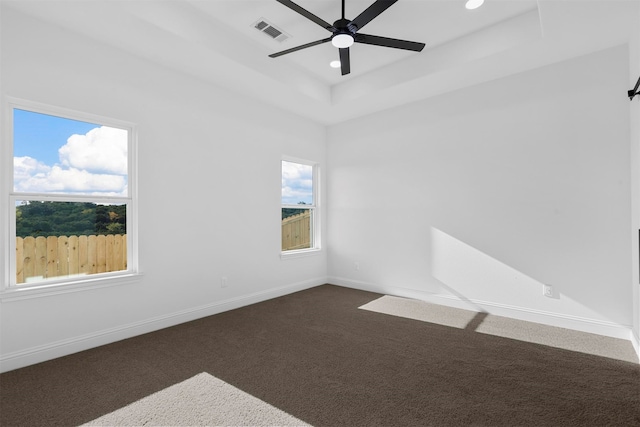 empty room with ceiling fan, a tray ceiling, and dark carpet