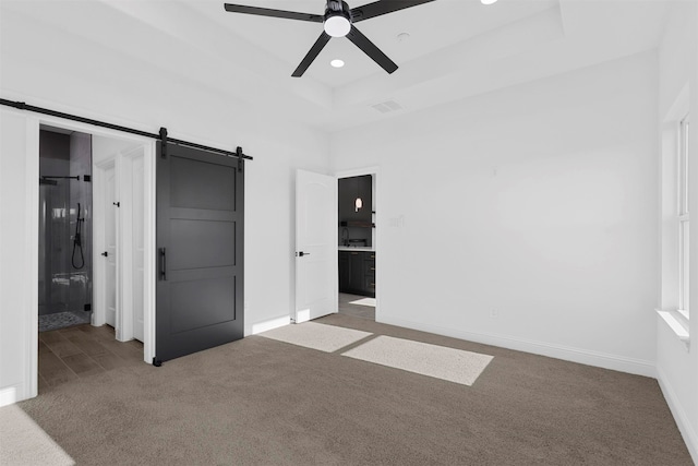 unfurnished bedroom with light carpet, a barn door, ensuite bathroom, and ceiling fan