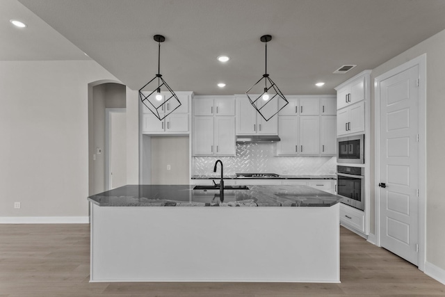 kitchen with arched walkways, under cabinet range hood, stainless steel appliances, a sink, and visible vents