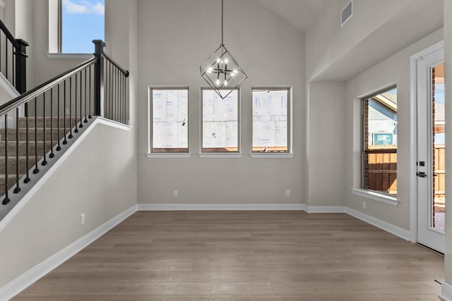 unfurnished dining area with wood finished floors, a towering ceiling, visible vents, baseboards, and an inviting chandelier