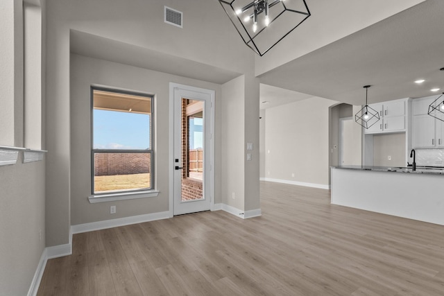 unfurnished living room with light wood finished floors, a sink, visible vents, and baseboards