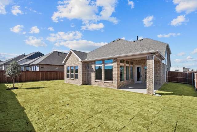 rear view of property featuring a patio, a fenced backyard, brick siding, a shingled roof, and a yard