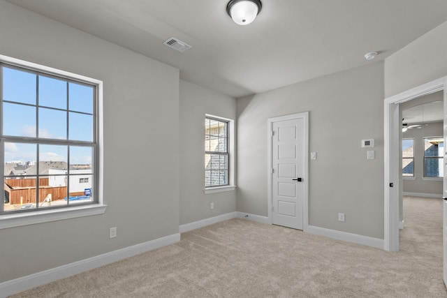 empty room with a healthy amount of sunlight, visible vents, and light carpet