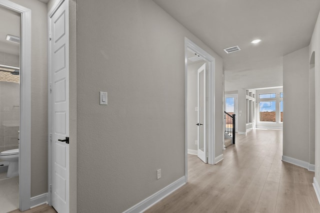 hallway with light wood finished floors, baseboards, visible vents, and arched walkways