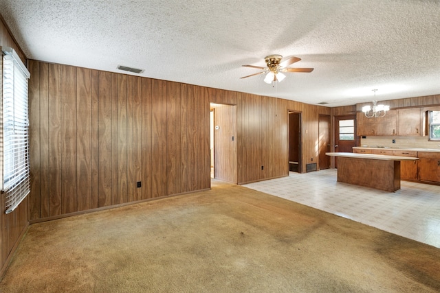 unfurnished living room featuring a textured ceiling, a healthy amount of sunlight, and wood walls