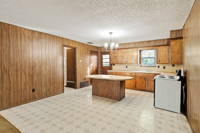 kitchen featuring wood walls, a kitchen island, pendant lighting, stove, and a chandelier