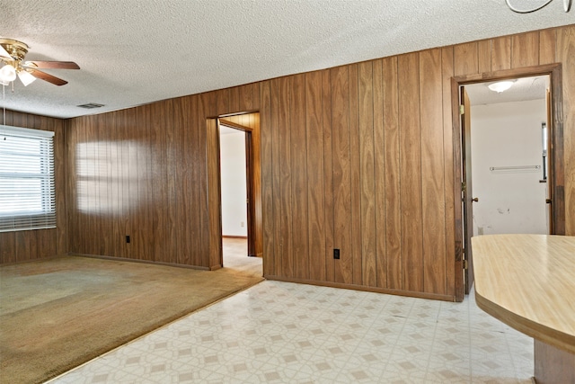 carpeted spare room featuring wood walls, a textured ceiling, and ceiling fan