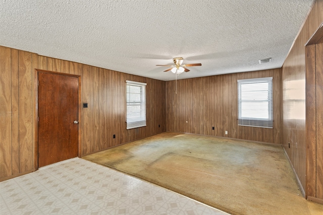 spare room featuring light carpet, a textured ceiling, wooden walls, and ceiling fan