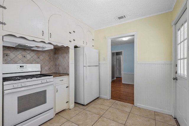 kitchen featuring premium range hood, light tile patterned flooring, white cabinets, white appliances, and a textured ceiling