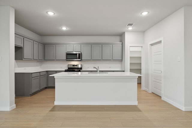 kitchen featuring gray cabinetry, sink, light hardwood / wood-style floors, stainless steel appliances, and a center island with sink