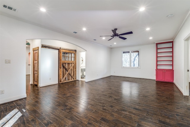 unfurnished living room featuring ornamental molding, a barn door, ceiling fan, and dark wood-type flooring