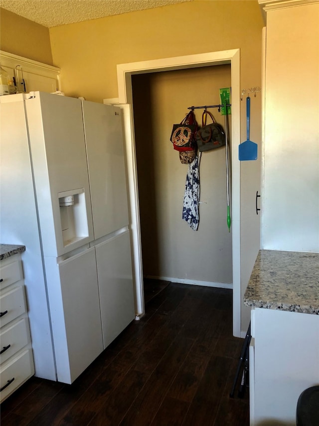 kitchen with dark wood-type flooring, white cabinets, a textured ceiling, and white fridge with ice dispenser