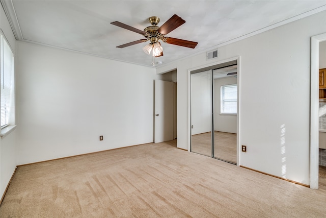 unfurnished bedroom featuring a closet, ceiling fan, light carpet, and crown molding