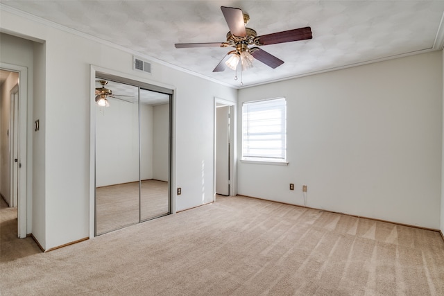 unfurnished bedroom featuring a closet, ceiling fan, light carpet, and crown molding