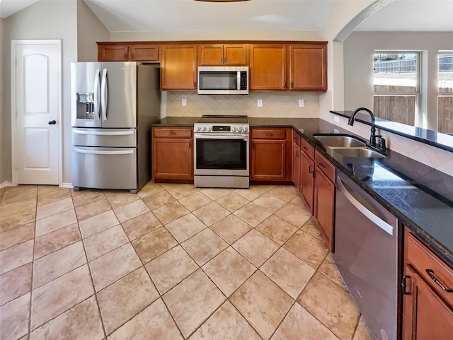 kitchen featuring lofted ceiling, backsplash, dark stone countertops, sink, and appliances with stainless steel finishes