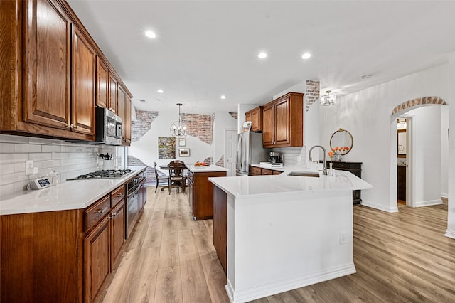 kitchen with sink, hanging light fixtures, kitchen peninsula, stainless steel appliances, and light hardwood / wood-style flooring