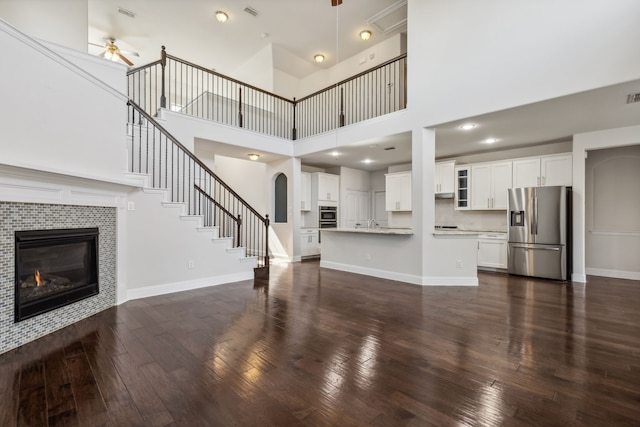 unfurnished living room with a tiled fireplace, a high ceiling, dark wood-type flooring, and ceiling fan