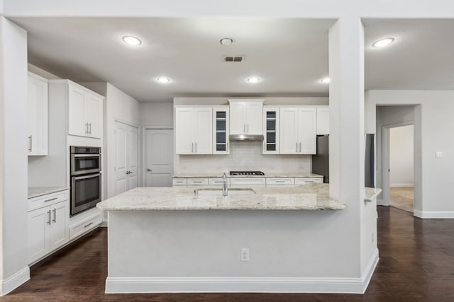 kitchen with light stone countertops, sink, white cabinets, and double oven