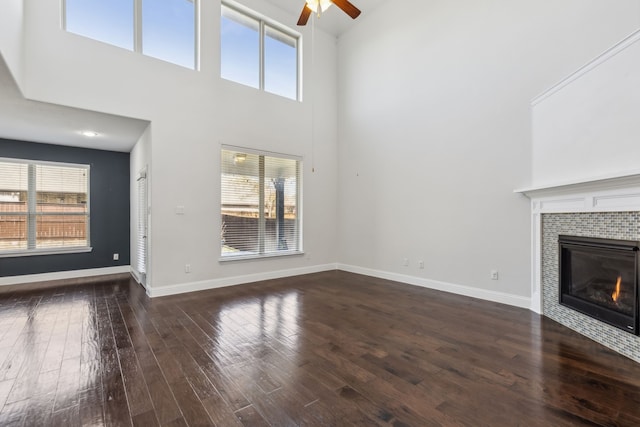 unfurnished living room featuring ceiling fan, a fireplace, dark hardwood / wood-style flooring, and a high ceiling