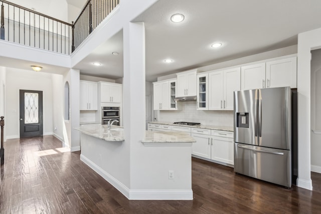 kitchen with dark wood-type flooring, appliances with stainless steel finishes, light stone countertops, and white cabinets