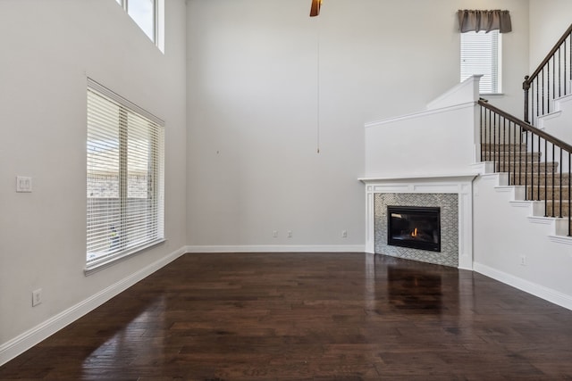 unfurnished living room featuring ceiling fan, dark hardwood / wood-style floors, a tiled fireplace, and a towering ceiling