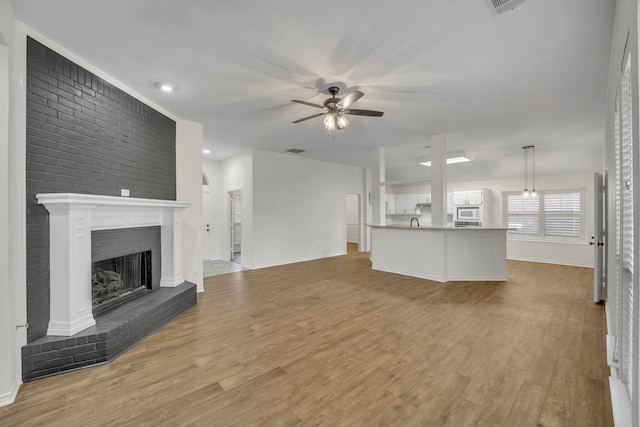 unfurnished living room featuring a brick fireplace, light hardwood / wood-style flooring, ceiling fan, and brick wall