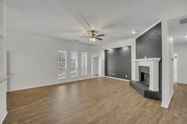 unfurnished living room featuring ceiling fan, wood-type flooring, and a brick fireplace